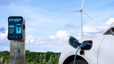 Elektrikli araba, rüzgar türbini çiftliğinde çalışan akıllı EV şarj cihazıyla şarj edilen enerjiyi şarj ediyor. Alternatif temiz sürdürülebilir enerjinin teknolojik ilerlemesi. İnceleyin