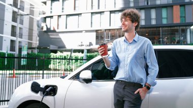 İlerici işadamı, şehir merkezinde dolaşmadan önce şarj cihazından elektrikli arabasına şarj prizi takıyor. Çevre dostu şarj edilebilir araba, sürdürülebilir ve temiz enerjiyle çalışıyor..