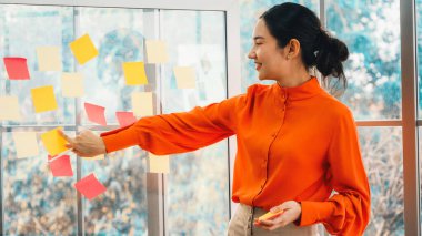 İş adamları ofisteki proje planlama kurulunda çalışıyor ve proje gelişimini analiz etmek için iş arkadaşlarıyla sohbet ediyorlar. Düzenli olması için cama yapıştırılmış yapışkan notlar kullanıyorlar. Jivy