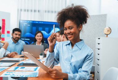 Bir grup ofis çalışanı ile birlikte arka planda ekranda gösterim paneliyle buluşan mutlu Afrikalı genç bir iş kadını portresi. Takım toplantısında kendine güveni tam bir ofis hanımı. Uyum