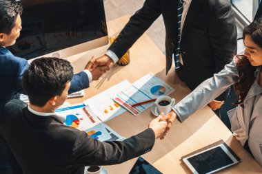 Grup iş adamları toplantı masasında el sıkışırken üst açıdan kendilerine güvenirler. Genç işadamı ve işkadını işçiler yatırım anlaşması imzaladılar. Jivy