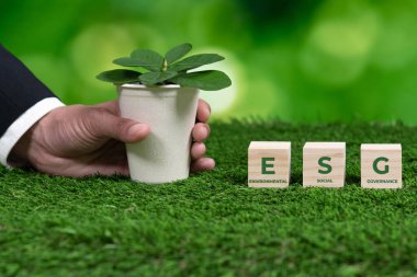 İş adamı elinde ESG küp sembollü saksı tutuyor. Orman yenilenmesi ve doğal farkındalık. Çevre dostu politikayla birlikte, ekolojiyi korumak için yenilenebilir enerji kullanan etik yeşil iş. Değiştir