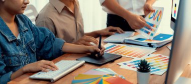 Grafik tasarımcısı, modern dijital stüdyo işyerinde profesyonel grafik ekibiyle benzersiz bir tasarım yaparken bilgisayar dizüstü bilgisayar ve grafik çizim kalemi üzerinde çalışır. Panorama çekimi. İnceleyin