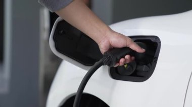 Adam garajdaki şarj istasyonundan elektrikli arabasını EV şarj cihazıyla şarj ediyor. EV arabaların teknolojik gelişimi ve gelecekteki sürdürülebilir enerji için ev enerjisi altyapısı. İnceleyin