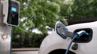 Doğal yeşil araba parkındaki ekolojik temiz enerji şarj istasyonundan gelen fütürist akıllı EV şarj aletinin şarj ettiği elektrikli araba. Alternatif enerji kullanan gelecekçi çevre dostu elektrikli araba. İnceleyin