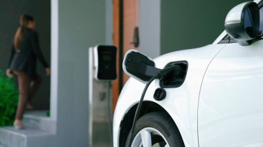 İlerici kadın evdeki elektrikli aracına şarj istasyonu fişi takıyor. EV otomobilleri çevreye yararlı temiz ve yeşil enerji kavramı sağlar.