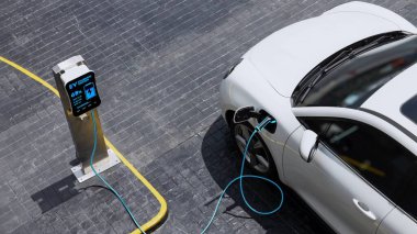 Şehir merkezindeki otoparktaki EV şarj istasyonundan hava görüntülü elektrikli araba şarj oluyor. Alternatif temiz ve sürdürülebilir enerji kullanan geleceğin yenilikçi yenilenebilir EV arabası. İnceleyin