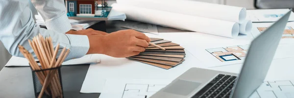 Interior architect designer at workstation table designing house interior blueprint and choosing mood board samples. Creative hand drawing sketch plan for house renovation or design concept. Insight