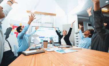 Bir grup ofis çalışanı toplantı odasında kutlama yapıyor, evrak işlerini havaya atıyorlar. İş adamlarından gelen heyecan ve özgürlük ifadesi, finansal analiz kağıtlarını kutlama jesti olarak fırlatıyor. Uyum