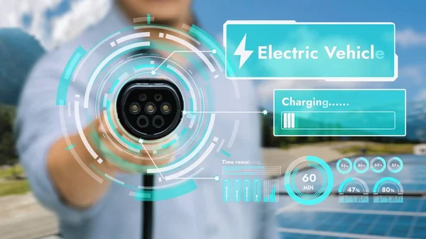 カメラの前にEv充電器を指す焦点手は ぼやけた緑色の発電機でスマートなバッテリー状態のホログラムを表示します Co2排出量を削減するクリーンエネルギーを使用した電気自動車充電器 Peruse — ストック写真