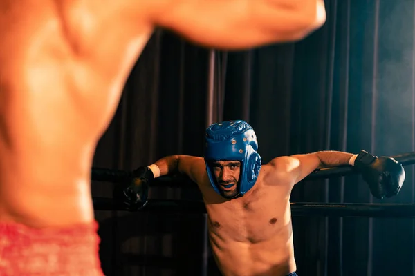 激しい激しい戦いでボクシングヘルメットとボクサーの戦闘機一方 競争相手は回復力と決意を示すリングに対して彼の背中と戦うために苦労しています インペトゥス — ストック写真