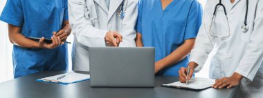 Tıbbi toplantıda doktor ve hemşire rapor ve dizüstü bilgisayarla birlikte stratejik tıbbi tedavi planını tartışıyorlar. Panoramik pankartta tıp fakültesi eğitim konsepti. Neoterik