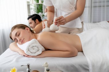 Sıcak bitkisel top spa masaj vücut tedavisi, masör nazikçe bitki torbasını çift müşteri vücuduna bastırıyor. Aromaterapi dinlenme sükuneti ve sükuneti kaplıca salonundaki atmosferi aydınlatıyor. Sessiz.