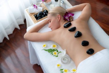 Lüks tatil köyündeki kaplıcalarda sıcak taş masajı. Gün ışığı sükunet ortamında, mutlu kadın müşteri bazalt taş masajından zevk alıyor. Rahatlatıcı bir sıcaklıkla vücudun üzerinde süzülüyor. Sessiz.