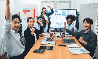 İş adamları TV ekranında başarılı bir sunum veya veri analizi toplantısından sonra kutlama yapıyorlar. Mutlu takım ofis odasında toplanıyor, kutlama jestleriyle işbirliği için tezahürat yapıyorlar. Uyum