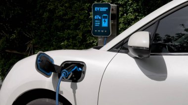 Elektrikli araba, çevre yeşil parkındaki elektrik kablosu ve yeşillik yeşili yeşillik yapraklarıyla şarj etmek için şarj istasyonuna bağlandı. Geleceğin yenilikçi her arabası ve enerji sürdürülebilirliği.