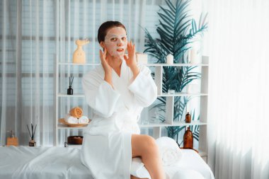 Kaplıca salonunun sakin, modern gün ışığı atmosferi, kadın müşteri poz veriyor ve yüz maskesi ile gençleştiriyor. Yüz bakımı ve güzellik kozmetolojisi prosedürü. Sessiz.