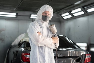 Tam korumalı ekipmanlı otomotiv işçisi sprey tabanca ya da oda atölyesindeki solunum cihazı boyasıyla araba kaportasına ustalıkla renk boyası uygular. Tamir için araba boyama servisi. Oxus.