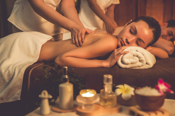 Caucasian couple customer enjoying relaxing anti-stress spa massage and pampering with beauty skin recreation leisure in warm candle lighting ambient salon spa at luxury resort or hotel. Quiescent