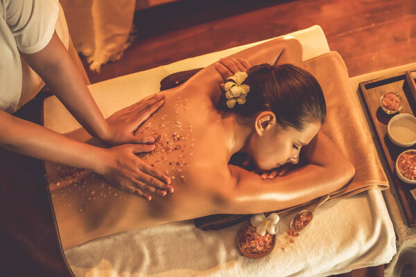 Woman customer having exfoliation treatment in luxury spa salon with warmth candle light ambient. Salt scrub beauty treatment in Health spa body scrub. Quiescent