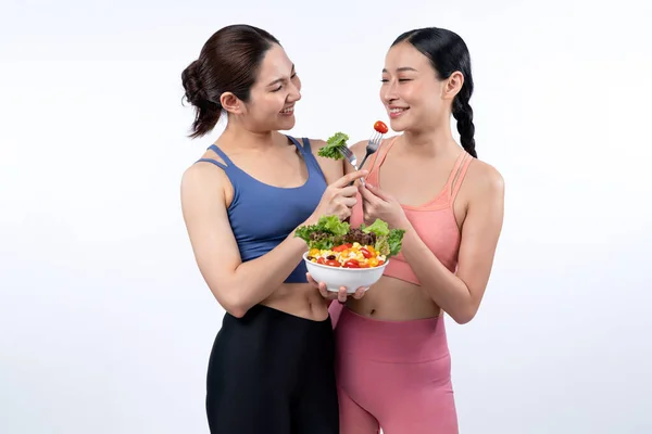 サラダボウルを保持しているスポーツウェアの2人の若いスポーティなアジアの女性は果物と野菜でいっぱいです 自然に若々しくフィットするボディライフスタイルの人々は 孤立した背景で栄養バランスをとっています ヴィゴーラス — ストック写真