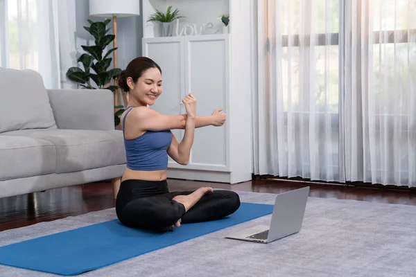 身穿运动服的亚洲妇女在健身垫上做瑜伽练习 以此作为她在家锻炼的常规 健康的身体护理生活方式女人在笔记本电脑上观看在线瑜伽视频 精力充沛的 — 图库照片