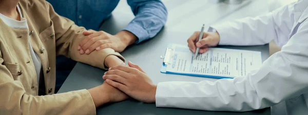 Arzt Der Mitfühlende Gesundheitsberatung Anbietet Während Junge Paarpatienten Händchen Halten — Stockfoto