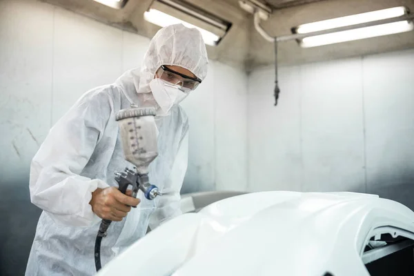 Automotive service worker in full protective gear expertly apply color paint in to cars bodywork with spray gun or respirator painting in chamber workshop. Car paint service for scratch refinish.Oxus