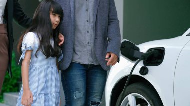 Elektrikli arabası ve şarj istasyonu olan yenilikçi bir genç aile ve kız. Sağlıklı çevre için elektrikli araçlardan gelen yeşil ve temiz enerji. Yenilenebilir kaynaktan eko güç.