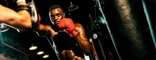 ジムでボクシングバッグトレーニング機器としてパンチングミットを身に着けているトレーナーやコーチでアフリカのボクサーパンチング プロボクシングの試合のための強さとスタミナトレーニング スプール — ストック写真