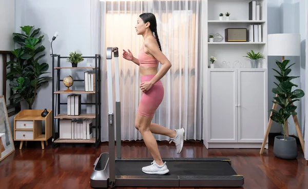 全长侧面看精力充沛 强壮的亚裔妇女在家里跑步的机器 追求健康的体形 致力于健康的生活方式 进行家庭锻炼和培训 精力充沛的 — 图库照片