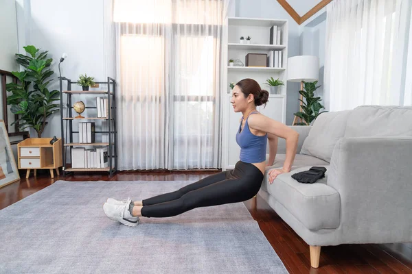 精力充沛 有决心的亚洲女人挺身而出躺在沙发上 以有效地控制胸部肌肉的增长 在家里追求健康的体形和致力于健康的生活方式 精力充沛的 — 图库照片