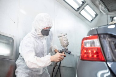 Tam korumalı ekipmanlı otomotiv işçisi sprey tabanca ya da oda atölyesindeki solunum cihazı boyasıyla araba kaportasına ustalıkla renk boyası uygular. Tamir için araba boyama servisi. Oxus.