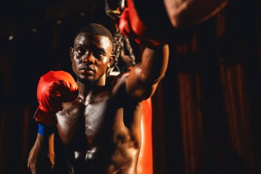 Afrika kökenli siyah boksör antrenöre yumruk atıyor ya da spor salonunda boks çantası olarak boks eldiveni takıyor. Profesyonel boks maçı için güç ve dayanıklılık eğitimi. Impetus