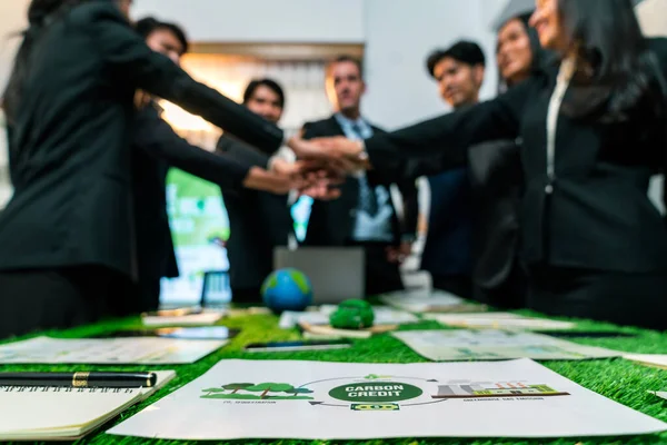 Environmental friendly idea paper on meeting table with blur background of business people holding hand together in synergy as team building concept to reduce CO2 emission for greener future. Quaint