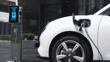 Şehir merkezinin otoparkındaki şarj istasyonuna bağlı elektrikli araba. Alternatif temiz ve sürdürülebilir enerji kullanan geleceğin yenilikçi yenilenebilir EV arabası. İnceleyin