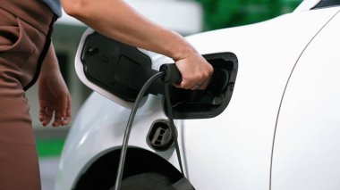 İlerici kadın evdeki elektrikli aracına şarj istasyonu fişi takıyor. EV otomobilleri çevreye yararlı temiz ve yeşil enerji kavramı sağlar.