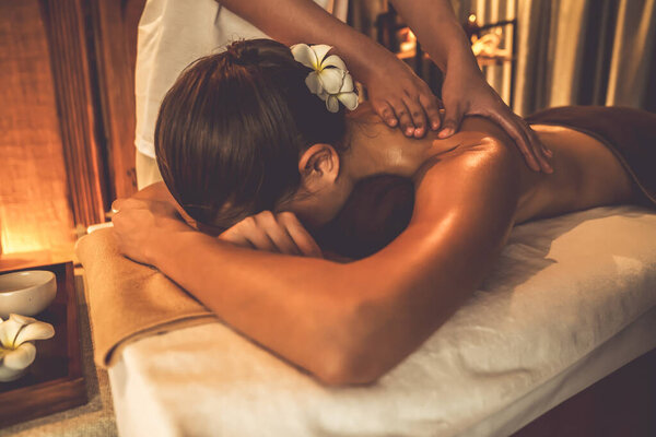 Caucasian woman customer enjoying relaxing anti-stress spa massage and pampering with beauty skin recreation leisure in warm candle lighting ambient salon spa at luxury resort or hotel. Quiescent