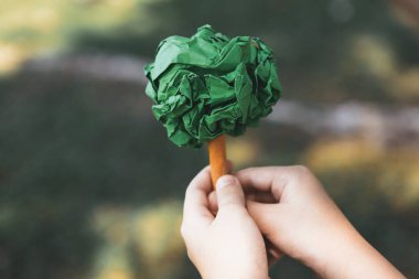 Geri dönüşümlü kağıt ağacı tutan küçük çocuk, gelecek nesiller için çevre yaşam tarzının azaltılması, yeniden kullanılması ve doğal olarak yeniden ağaçlandırılması ve uzun vadeli çevresel sürdürülebilirlik konularında destek veriyor. Döngü