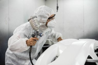 Tam korumalı ekipmanlı otomotiv işçisi sprey tabanca ya da oda atölyesindeki solunum cihazı boyasıyla araba kaportasına ustalıkla renk boyası uygular. Tamir için araba boyama servisi. Oxus.
