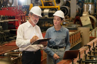 Metal imalatında makine mühendisliği denetleyicisi olarak liderlik örneğini sunan çelik endüstriyel makineyi incelemek için dizüstü bilgisayar kullanan fabrika mühendisi ve asistan..