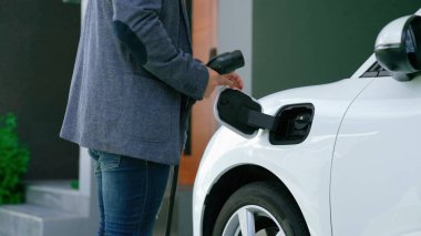İlerici adam evindeki elektrikli aracın aküsüne emisyonsuz güç bağlantısı kuruyor. Elektrikli araç elektrik istasyonundan EV araba aküsüne kabloyla şarj oluyor.