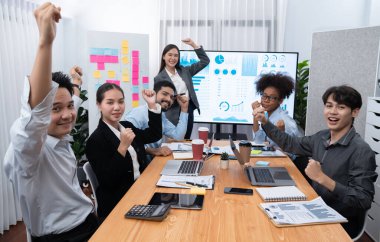 İş adamları TV ekranında başarılı bir sunum veya veri analizi toplantısından sonra kutlama yapıyorlar. Mutlu takım ofis odasında toplanıyor, kutlama jestleriyle işbirliği için tezahürat yapıyorlar. Uyum