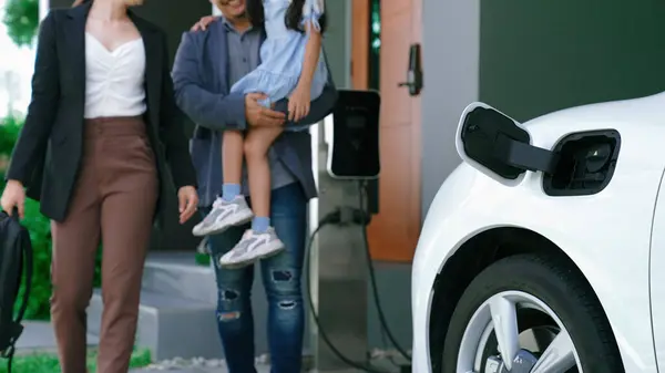 年富力强的年轻父母和女儿住在有电动汽车和电动汽车充电站的家里 促进健康环境的电动汽车的绿色清洁能源 — 图库照片