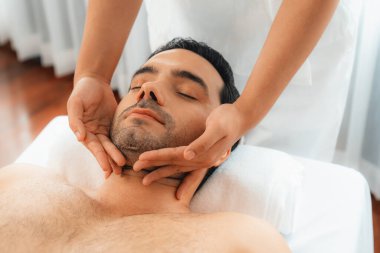 Beyaz adam stres önleyici kafa masajından ve lüks bir tatil beldesi veya otel spa salonundaki modern ışık ortamında yüz güzelliği eğlencelerini şımartmaktan hoşlanıyor. Sessiz.