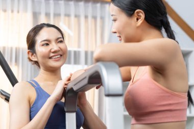 Enerjik ve güçlü atletik Asyalı kadın evde spor arkadaşı ya da antrenörü ile birlikte eliptik koşu makinesiyle koşuyor. Formda fiziğin takibi ve sağlıklı yaşam tarzına bağlılık. Kuvvetli