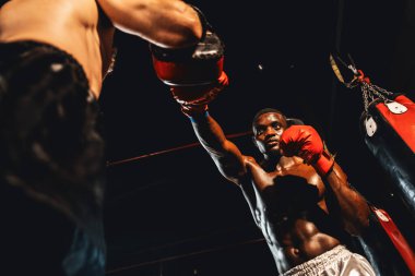 Afrika kökenli siyah boksör antrenöre yumruk atıyor ya da spor salonunda boks çantası olarak boks eldiveni takıyor. Profesyonel boks maçı için güç ve dayanıklılık eğitimi. Impetus