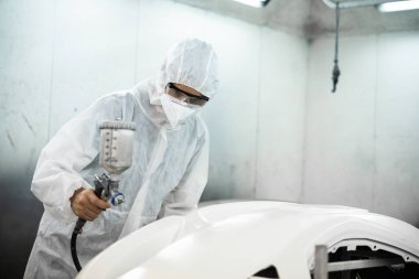 Tam korumalı ekipmanlı otomotiv işçisi sprey tabanca ya da oda atölyesindeki solunum cihazı boyasıyla araba kaportasına ustalıkla renk boyası uygular. Tamir için araba boyama servisi. Oxus.