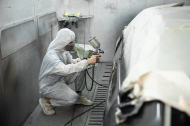 Tam korumalı ekipmanlı otomotiv işçisi sprey tabanca ya da oda atölyesindeki solunum cihazı boyasıyla araba kaportasına ustalıkla renk boyası uygular. Tamir için araba boyama servisi. Oxus.