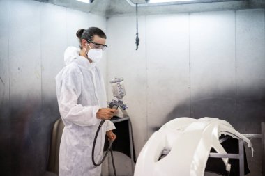Koruyucu ekipmanlı otomotiv işçisi araba kaportasına sprey tabanca ya da oda atölyesindeki solunum boyasıyla renk boyası uyguluyor. Tamir için araba boyama servisi. Oxus.